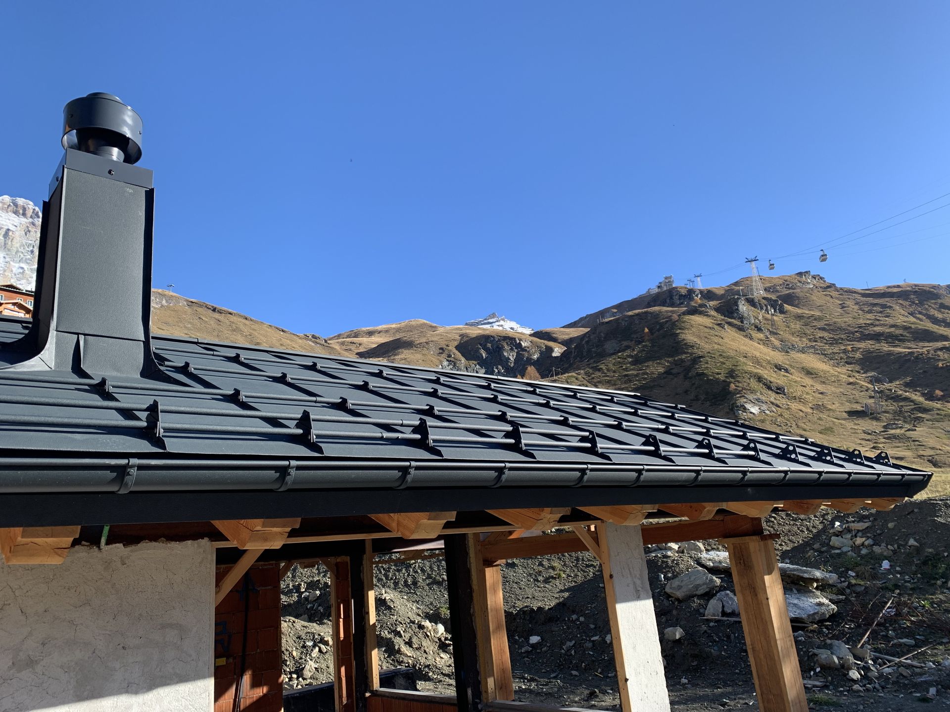 Copertura in lamiera scura con fermaneve e camino, sullo sfondo le montagne